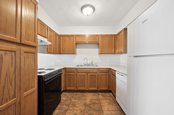 An empty kitchen with wooden cabinets and white appliances